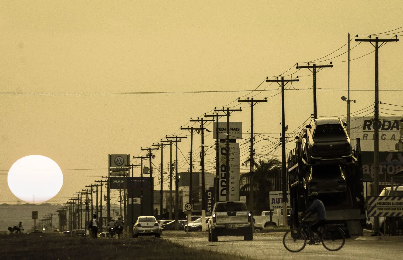 Avenida comercial de Vilhena ao pôr do sol, com lojas e caminhões